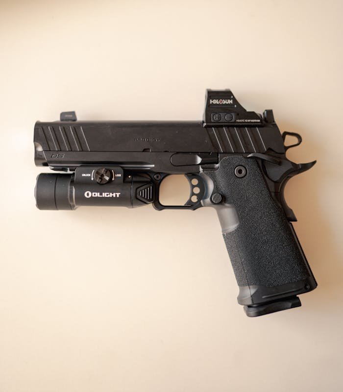 The Art of Drawing Readers In: Your attractive post title goes here Close-up of a tactical handgun equipped with a mounted light and holographic sight on a neutral background.